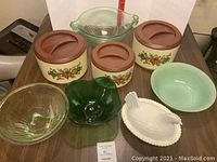 Overview photo showing 3 decorated Sterilite canisters with brown lids, 4 glass bowls of varying sizes and colors, and white ceramic chicken bowl arranged on table