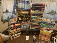 Overview of VHS tapes stacked on table showing Disney movies, World War II series, Die Hard, John Wayne and other VHS titles along with the player.