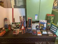 Full overview of assortment of tools neatly arranged on table including paint brushes, tape measures, scissors, repair kits, extension cord, and more.