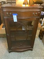 Front view of dark wood display cabinet with glass door and drawer, showing overall structure and design.