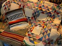 Vintage hand sewn colorful patchwork quilt with scalloped edges overlaid with two woven blankets in multi-color and black/white stripes with fringe edges.