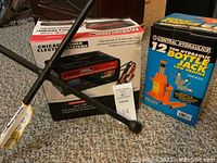Photo showing Chicago Power Electric Systems battery charger and engine starter in original box along with CeFtral Hydraulics 12 ton bottle jack box and a black lug wrench crossed in front.