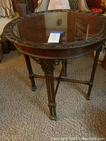Full view of round wooden table with glass insert on top, showing decorative edge and wooden legs.