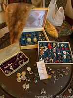 Full view of jewelry collection displayed on a round table including multiple boxes and trays with clip-on and screw-back earrings and rings.