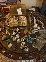 Wide view of assorted pins, bracelets, and necklaces spread on a round table with some pieces in a padded box