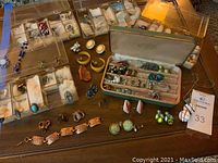 Wide shot of costume jewelry including pins, clip-on earrings, necklaces, and rings displayed on a table with jewelry trays and a jewelry box.