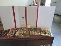 Wide shot showing multiple beaded necklaces and numerous compartments filled with clip-on earrings and pins in plastic organizer boxes.