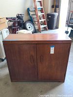 Full view of vintage wooden record cabinet with two doors, showing overall condition and size context in garage environment.