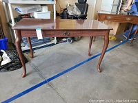 Full view of the wooden sofa table showing four curved legs and a rectangular top with a handle on front.
