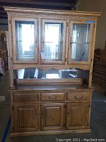 Full view of the assembled two-piece china cabinet showing glass hutch on top and wooden base with drawers and doors.