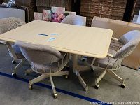 View of rectangular dining table with removable leaf and four upholstered rolling chairs arranged around it.
