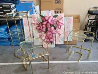 Photo showing the five glass top tables with brass frames arranged alongside the multi-panel painted canvas wall art with pink floral design in the background.