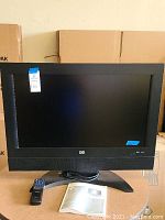 Front view of the HP LC3260N 31" LCD HDTV with remote and user guide on table.