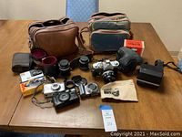 Full lot on table showing assortment of cameras, lenses, flash, bags, manual and film boxes