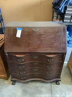 Front view of closed drop-front secretary desk showing serpentine drawer fronts and brass hardware