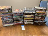 Four stacks of DVDs arranged on a wooden table, showing a wide variety of movie titles.