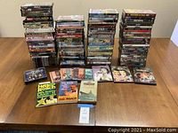 Full lot arranged with stacks of DVDs in original cases, music CDs, and three books arranged front and center.