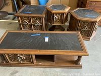 Four wooden tables featuring black textured stone tops with carved wood frames and ornate metal hardware handles, visible wear and damage, photo taken to show full set condition and design