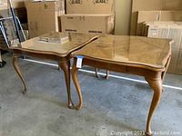 Two matching oak tables with parquet pattern tops covered with glass. One table includes a drawer on one side. Tables have curved legs and are in good condition.