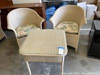 Two off white wicker armchairs with floral cushions and matching wicker square table with glass top.