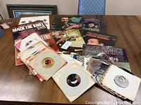 Wide shot of table with vintage LP records and a large stack of 45 RPM singles in paper sleeves.