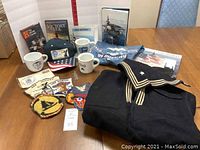 Full lot shot showing US Navy uniform, USS Midway patches, sailor cap, mugs, books, DVDs, and T-shirt.