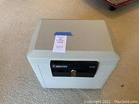 Full view of the closed Sentry Safe on carpeted floor showing exterior color and shape with taped auction tag.