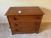 Front view of wooden cedar chest of drawers with three drawers and rounded wooden knobs on carpeted floor.