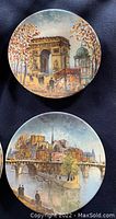 Front view of two collector plates showing detailed scenic cityscape artwork, one plate with Arc de Triomphe and another with a river bridge and city skyline