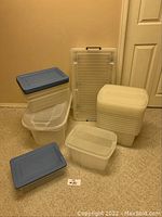 Photo showing 16 plastic organization bins in varying sizes including two with blue lids and the rest with clear or translucent lids.