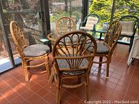 Dining set viewed from side showing five rattan chairs with curved back designs and the glass tabletop above the rattan table base.