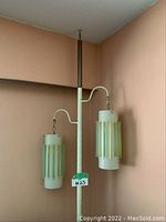 Full view of tension-mounted floor to ceiling lamp with two pendant shades against pink wall