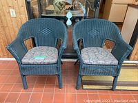 Front view of two dark green plastic rattan chairs placed side by side with patterned seat cushions.