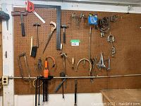 Tools hanging on pegboard wall including saws, hammers, clamps, a hedge trimmer and brushes.