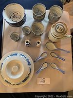 Top-down view of the full dish set arranged on a table showing all items including bowls, cups, teapot, spoons, shakers, covered serving dish.