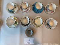 Top view of all 9 teacups and matching saucers opposite to each other in two rows, showing different floral designs and gold rim accents.