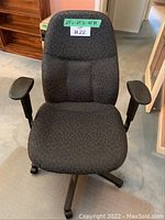 Front view of black desk chair showing padded backrest, armrests, and five caster wheeled base.