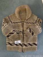 Front view of beige and brown Cowichan sweater with wide shawl collar and zipper closure.