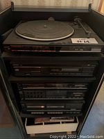 Front view of stacked Sanyo stereo components inside black cabinet with glass top showing record player.