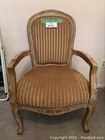 Front view of beige armchair showing upholstery, carved wooden frame with floral detail, and dimensions.