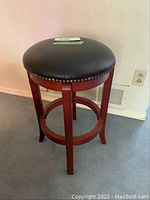 Full view of the swiveling barstool showing black cushioned seat and wooden legs.