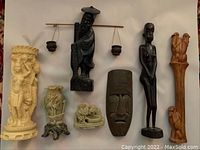 All 7 sculptures displayed on a flat surface showing ivory-toned, dark wood, and stone pieces.