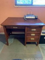 Front view of wood desk showing four drawers on the right and one drawer in the center with gold hardware handles.