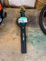 Top view of the leaf blower on the floor showing elongated nozzle and the extension cord plugged in.