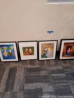 Photo showing four framed animated movie art posters on the floor against a wall, each with distinct cartoon-style scenes.