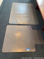 Two clear textured plastic office chair mats on carpet with one larger rectangular mat and one smaller contoured mat next to a wooden desk.