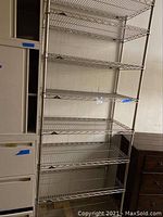 Front view of tall metal wire shelving unit with six shelves against a wall.