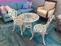 Round white metal table and two matching chairs on a blue carpet indoor setting, showing full set.