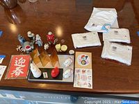 Photo showing the arrangement of five metal robot figurines, Asian decorative figurines on black tray with gold folding screen, red calligraphy art, paper doll art, stickers, and four white T-shirts with tags.