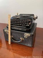 Front side view of Remington 5 typewriter on carrying case with a ruler beside it for scale.